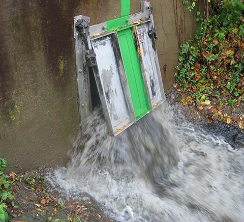 Stormwater overflowing out of a metal and wood door into an outside runoff area